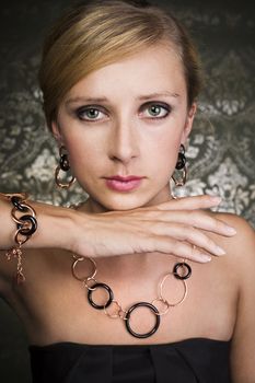 elegant woman wearing golden necklace and earrings, over wallpaper background