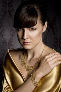 portrait of elegant woman wearing golden necklace and bracelet, over wallpaper background