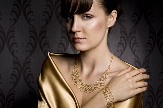 portrait of elegant woman wearing golden necklace and bracelet, over wallpaper background