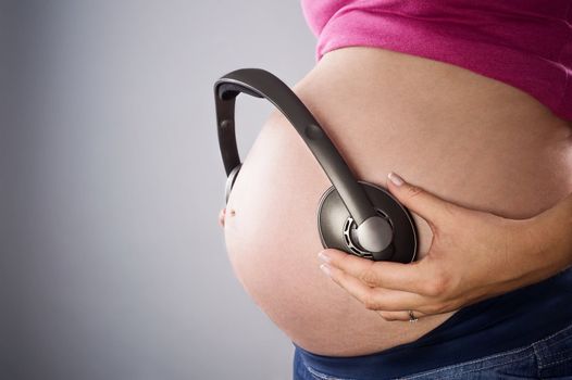 pregnant belly and earphones over gray background