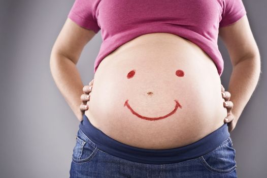 pregnant female with smile on belly over gray background