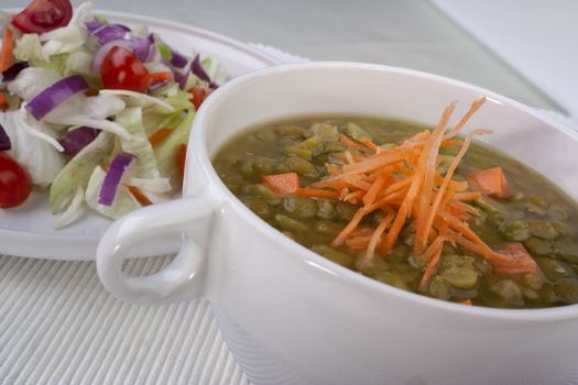 Close up of pea soup with carrots and side salad. 