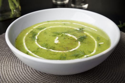 Fresh pea soup in white bowl seasoned with dill, cream and pepper.