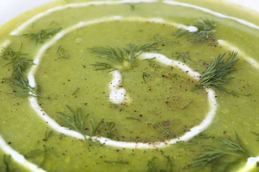 Close up of fresh pea soup with cream, dill and seasoned with pepper.
