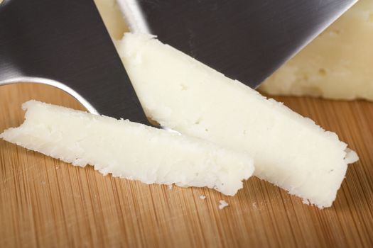 Close up of  large shreds of Italian cheese with cheese slicer.