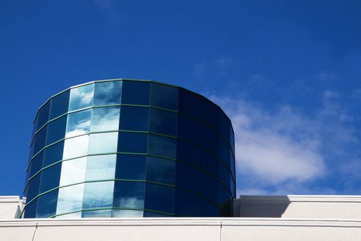 Angled reflective windowed Cylinder Building reflecting blue sky and clouds