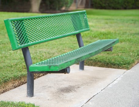 Green metal bench with shallow dept of field against green grass in park