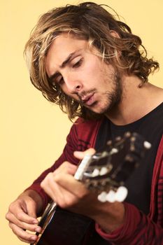 Young handsome Caucasian man playing the guitar and whistling (Selective Focus, Focus on the left eye)