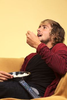 Young man watching TV and eating popcorn (Selective Focus, Focus on the left side of the face)