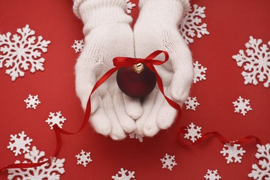 christmas ball in hands on red background with snowflakes