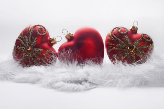 three christmas heart shaped balls on white feather background