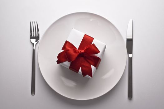 gift with decorative red ribbon on a dinner plate on white background