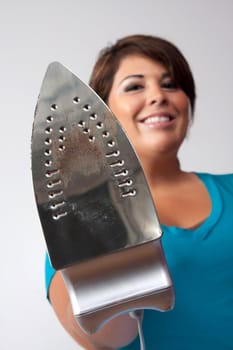 A young woman at home holding up her household iron with a happy grin isolated over a silver background.