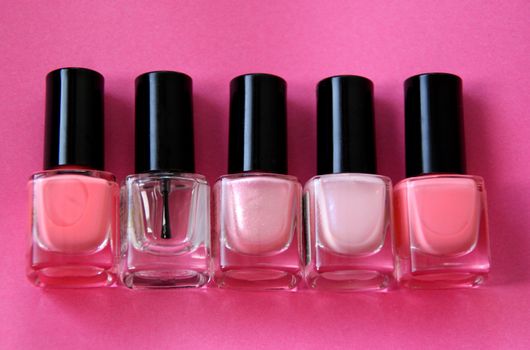 Five bottles of nail polish over a pink background.