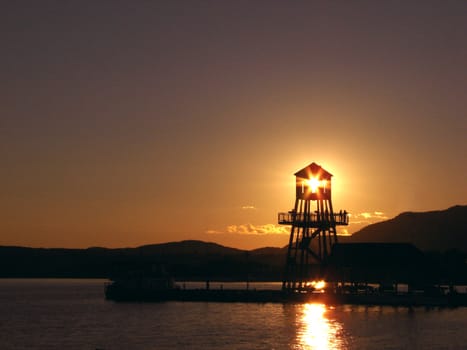 Observation tower in silhouette at sunset on Memphremagog lake, in Magog, province of Quebec, Canada, with Mont-Orford in background