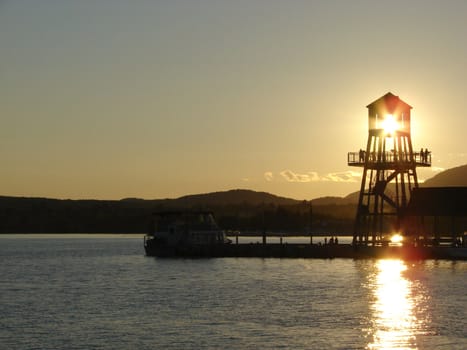 Observation tower in silhouette at sunset on Memphremagog lake, province of Quebec, Canada, with Mont-Orford in background