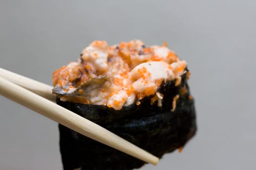 sushi with chicken taken with chopsticks on gray background