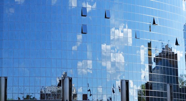 a mirror reflection of sky and clouds is in the windows of building