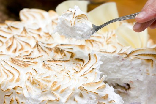 fresh meringue cake and the hand with piece of it in the spoon