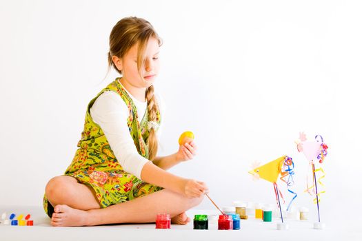 Studio portrait of a young blond girl who is painting easter eggs