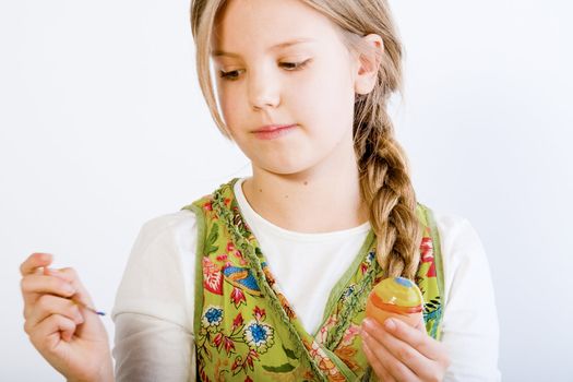 Studio portrait of a young blond girl who is painting eggs for easter