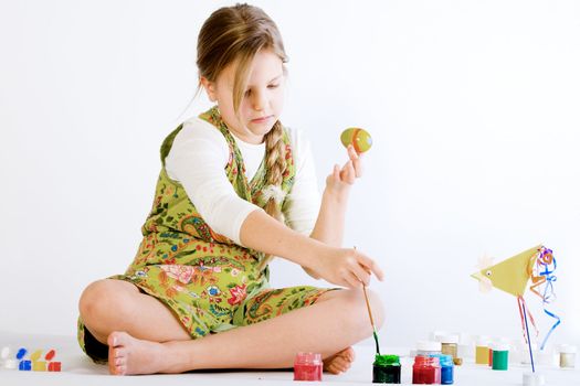 Studio portrait of a young blond girl who is playing with paint and eggs for easter