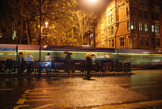 A city tram speeds through the city on a rainy evening