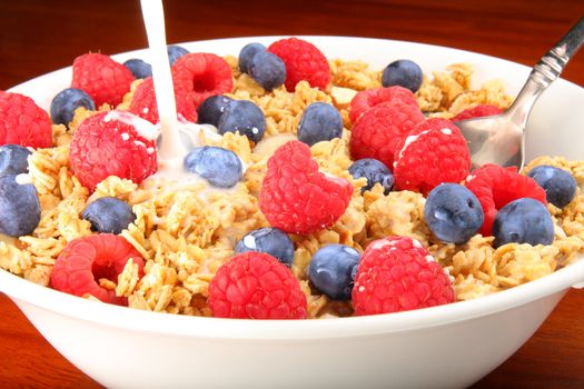 Delicious bowl of granola cereal with raspberries, blueberries and milk