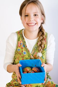 Studio portrait of a young blond girl who is presenting a blue box with her painted easter eggs