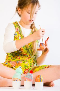 Studio portrait of a young blond girl who is painting easter eggs