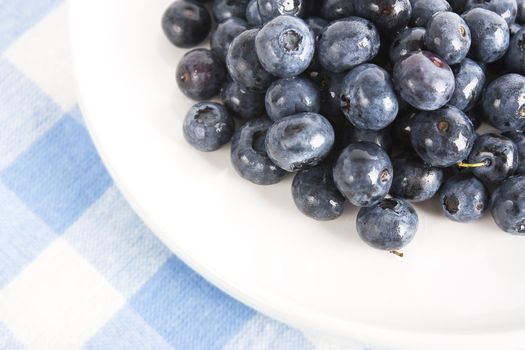 Closeup of blueberries on white plate and blue and white linen tablecloth