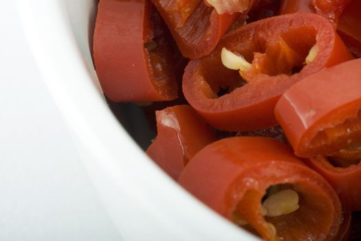 Macro photo of sliced red chili peppers in white bowl.  