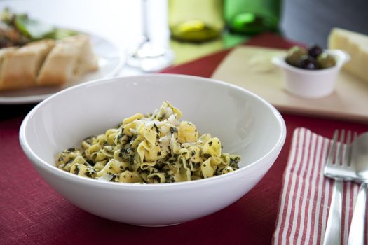 Perline pasta with pesto sauce on table with salad and olives.