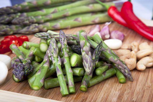 Asparagus, cashews, garlic and hot peppers on cutting board ready for a stir fry.