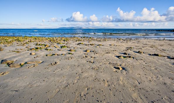 Galway Bay in Ireland. The photo is layered with sand, water, The Burren (hills), and sky.