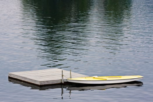 A small yellow boat tied to a dock on a lake.