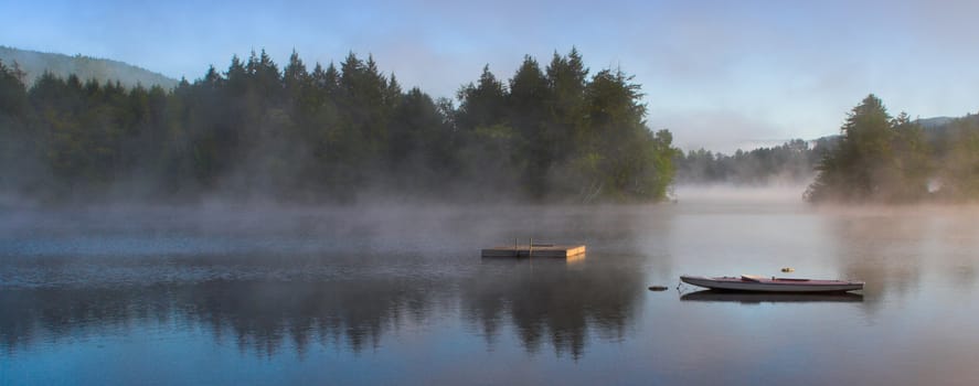 A lake in the early morning with rising fog. Panorama format.