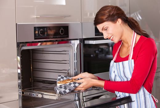 Attractive young woman taking her baked cake out of the oven