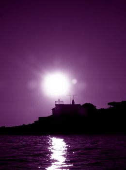 Silhouette of an old lighthouse at sunset time , black and white purple toned photo