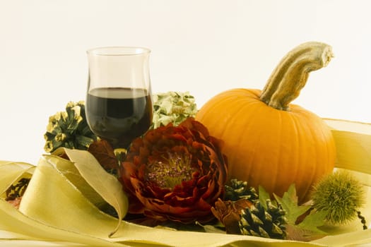 Red wine in an autumn tone glass in a celebratory still life with an orange pumpkin, red blossom, seasonal chestnut burr, pine cone and dry leaves offer an elegant toast to the celebration of autumn