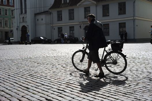 RIGA, LATVIA - AUGUST 9: Man walking his bicycle on an old cobblestone road in Old Town of Riga on August 9, 2010