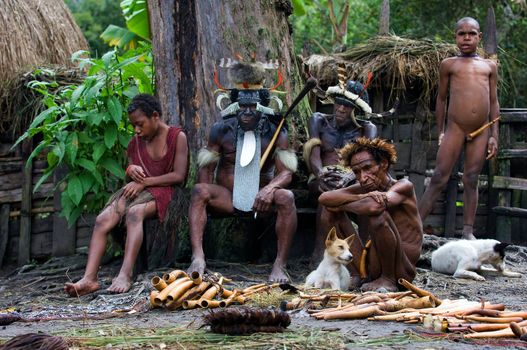 New Guinean natives Dani of a tribe sit on a bench in the village.