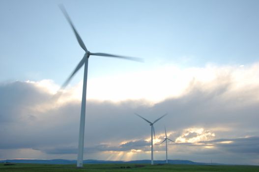 Wind turbine farm near Lethbridge, Alberta, Canada.  Picture taken to show movement in the blades with stormy, fluffy clouds in background with sun shining through them in the eveing.