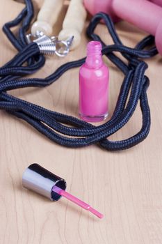 Pink open nail polish standing by a jump rope and a pink dumbbell.