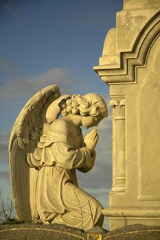 angel sculpture praying in front of stone tomb, yellow dusk sun
