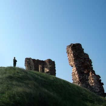 solitary man standing on top of a hill and looking at castle ruins