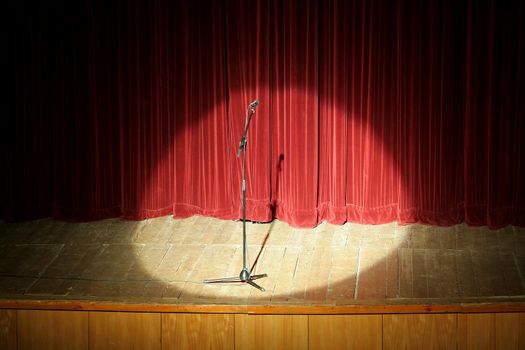 microphone on wooden stage, red curtain in background, spot light