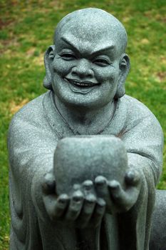 stone buddha sculpture offering a cup and smiling, grass in background