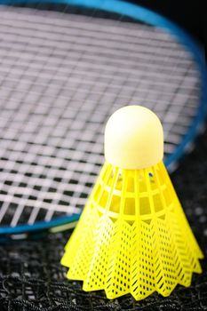 Bright yellow badminton shuttlecock and blue racquet laying on a badminton net.