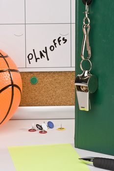 A silver whistle on a green notebook next to an orange basketball and a calendar with the date of the playoffs on it.